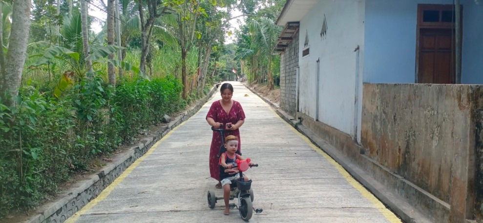 Jalan Rabat Beton TMMD Jadi Tempat Nyaman, Ibu Marisa Momong Anak dengan Sepeda